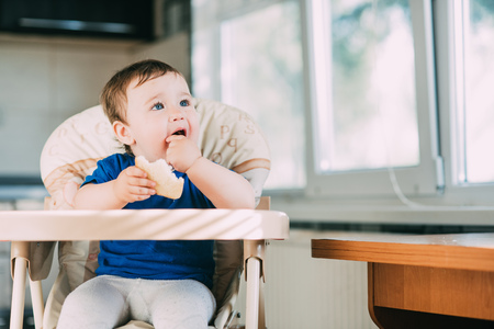 Baby girl is very greedy eating a piece of white bread, hungry and happy