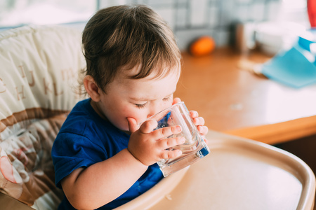 A little girl in the kitchen in the afternoon in a high chair drinking waterの写真素材
