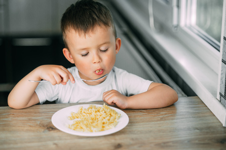 a little boy eats pasta in the form of a spiral in the afternoon in the kitchen on their own very appetizingの写真素材