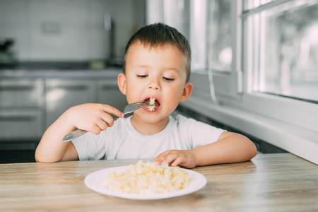 a little boy eats pasta in the form of a spiral in the afternoon in the kitchen on their own very appetizingの写真素材