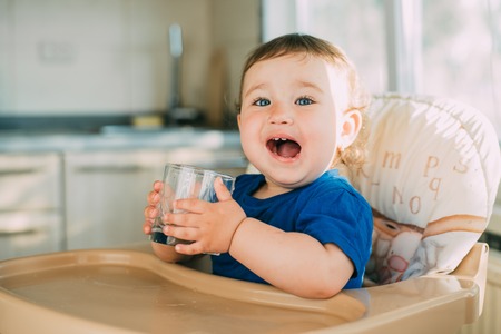 A little girl in the kitchen in the afternoon in a high chair drinking waterの写真素材