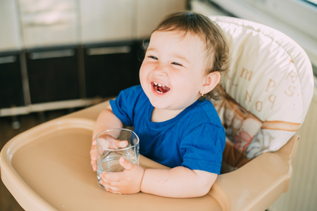 A little girl in the kitchen in the afternoon in a high chair drinking waterの写真素材