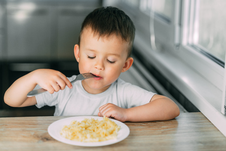 a little boy eats pasta in the form of a spiral in the afternoon in the kitchen on their own very appetizingの写真素材