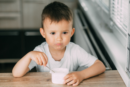 Lovely little boy eating yogurt in the kitchen during the day very appetizingの写真素材