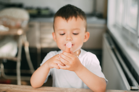 Portrait of a adorable little boy in a white t-shirt at the table eating a sausageの写真素材