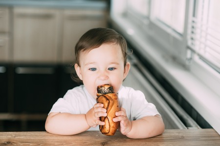 a little girl in the kitchen during the day eating a bun with poppy seeds is very appetizing and greedyの写真素材