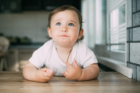 A charming little girl climbed on the table and eats a sausage withの写真素材