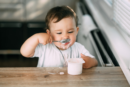A small, cheerful, charming girl eats yogurt all smeared herselfの写真素材