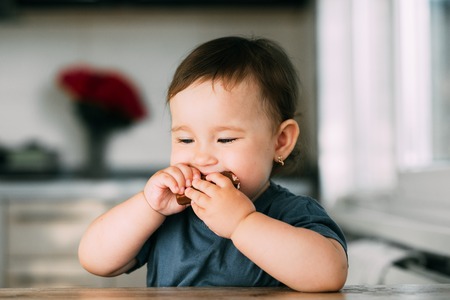 little beautiful girl in the afternoon in the kitchen eating a delicious chocolate barの写真素材