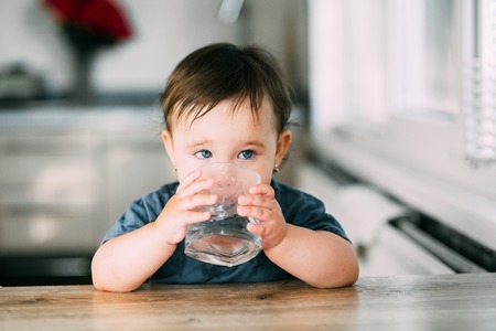 Cute little girl sitting in a baby chair in the kitchen and drinking water