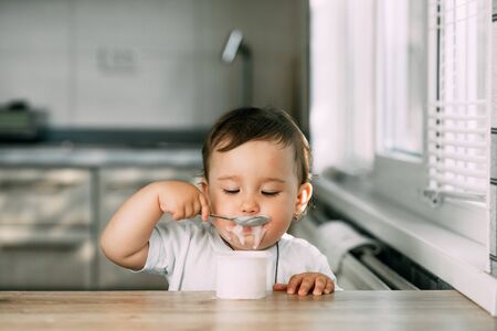 A small, cheerful, charming girl eats yogurt all smeared herselfの写真素材