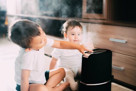 Children, brother and sister near humidifier, from which goes steam.The concept of humidity in the houseの写真素材