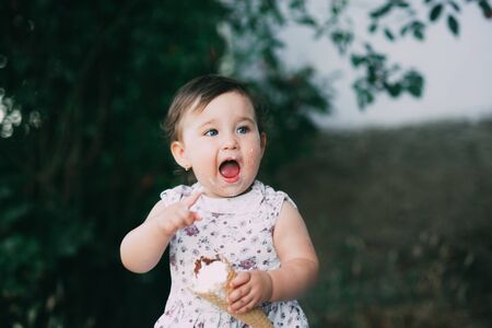 Little, charming girl in dress in summer eating ice cream at sunset, very cuteの写真素材
