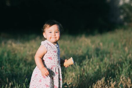 Little, charming girl in dress in summer eating ice cream at sunset, very cuteの写真素材