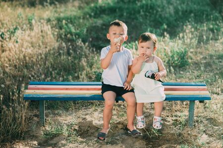 Brother and sister eating ice cream on the bench in the Playground