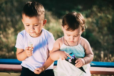 Brother and sister eating ice cream on the bench in the Playgroundの写真素材