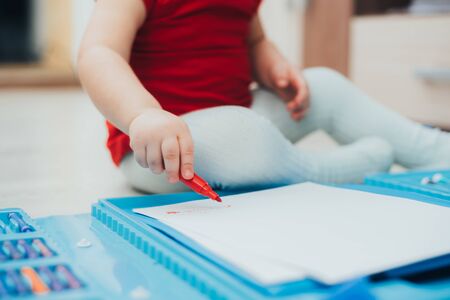 A little girl in a red t-shirt is drawing with a red marker on a blue easel cuteの写真素材