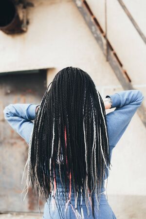 Girls standing in a blue suit with black Afro pigtails on the background of an old building with their backs to the camera coolの写真素材