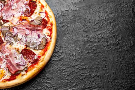 DIABLO pizza on a black background, tomato-based Pizza with mozzarella, veal, bacon, Napoli salami, onion and chili pepper on a wooden standの写真素材