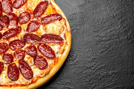 PEPPERONI pizza on a black background, tomato-based with mozzarella and spicy salami Napoli on a wooden standの写真素材