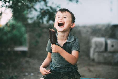Boy eats ice cream on a stick covered with chocolate, outdoors cute
