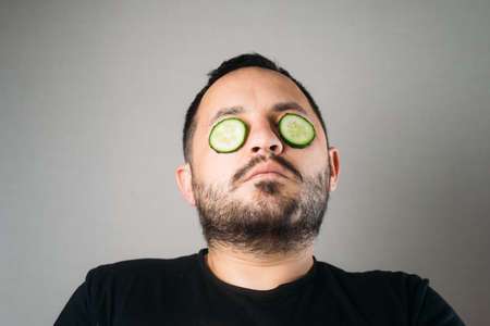 Relaxed bearded young man with a hydrating cucumber mask on his face fun