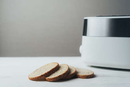 A white and silver toaster sits on a white wooden table with slices