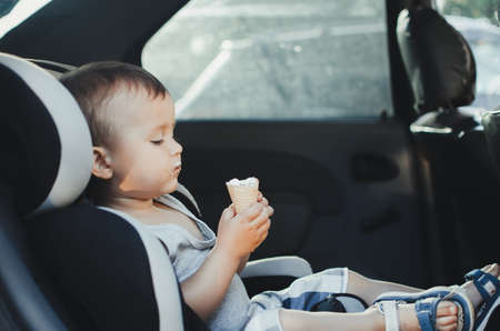 A small child eating ice cream, sitting strapped in the car seatの写真素材