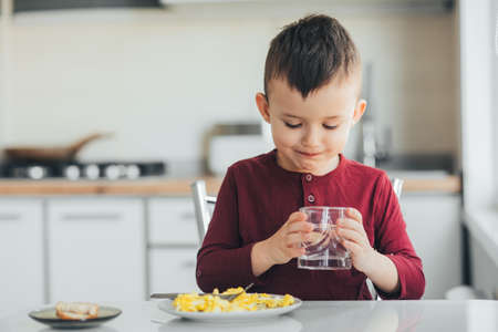 A child in the afternoon in a white light kitchen drinks waterの写真素材