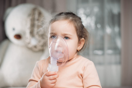 little cute girl sitting on the bed in the bedroom doing inhalationの写真素材