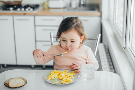 Baby in the afternoon in the white light kitchen in a pink sweater eating an omeletの写真素材