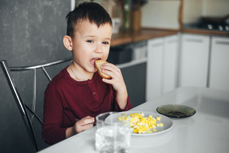 Boy in the kitchen eating bread on the table omelet in a plateの写真素材