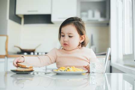a cute girl in the kitchen is eating breadの写真素材