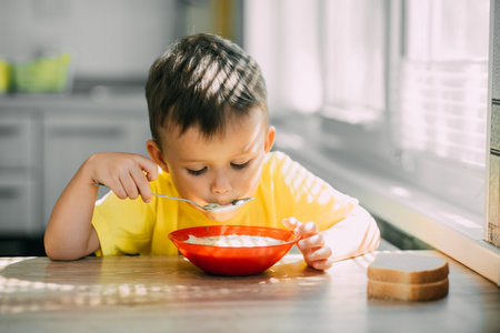 A child in a yellow t-shirt in the kitchen eating a national Russian dish called Okroshkaの写真素材