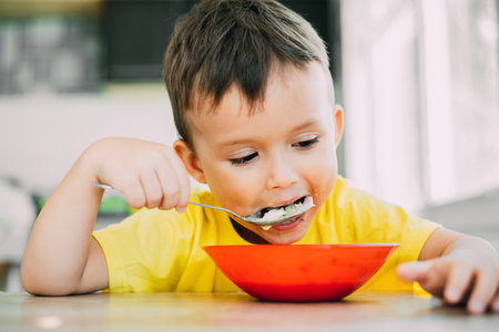 A child in a yellow t-shirt in the kitchen eating a national Russian dish called Okroshkaの写真素材