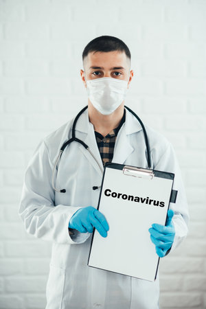 Doctor with clipboard on a white background with a pen shows the name of the disease Written in red coronavirusの写真素材
