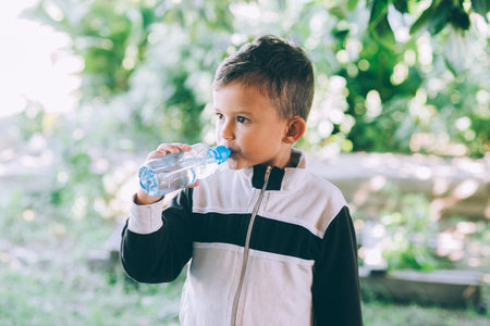 A little boy drinks water outdoors from a blue bottleの写真素材