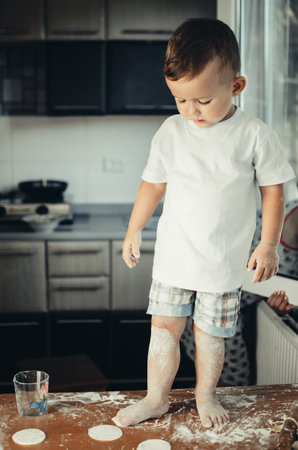 The child is standing on the kitchen table covered in flourの写真素材