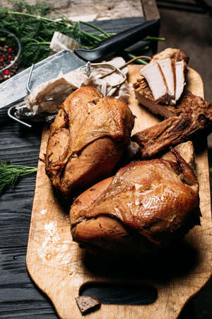 homemade hot smoked chicken breast, on an old wooden board next to vegetables and spicesの写真素材