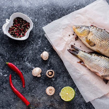 Fresh carp fish top view on paper and black granite background , mushrooms , herbs and lime spices...
