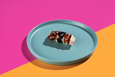 A plate of sushi sits on a blue plate with a pink background. The sushi is covered in black sauce and is the main focus of the imageの写真素材