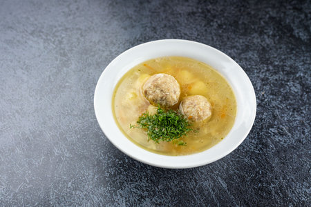 Delicious homemade soup with meat meatballs and fresh herbs in a white plate. Delicious first course with broth, potatoes, carrots and spices.の写真素材