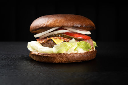Juicy potato bun cheeseburger on a black background with ham, beef cutlet, greens and vegetablesの写真素材