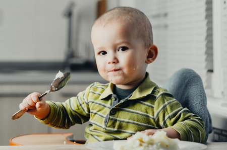 The child in the kitchen alone with a spoon eats mashed potatoesの写真素材