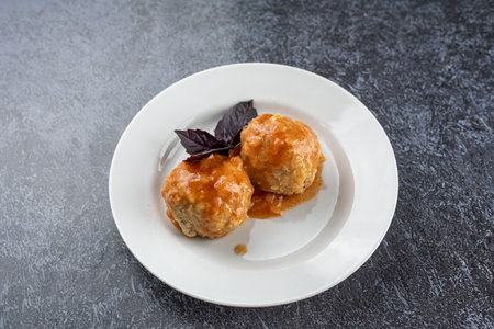 A plate of meatballs with a sprig of basil on top. The plate is white and the meatballs are redの写真素材