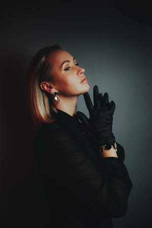 A woman in a black dress is wearing gloves and standing in front of a wall. She is wearing a watch and earringsの写真素材