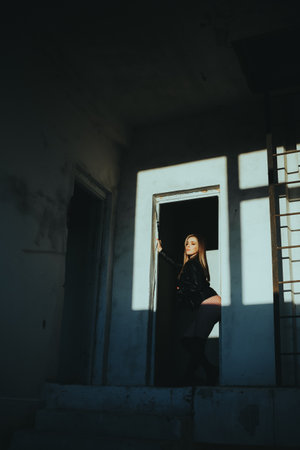 A woman stands in front of a door, looking out into the hallway. The room is dimly lit, and the woman's silhouette is cast against the wall. Scene is somewhat eerie and mysteriousの写真素材