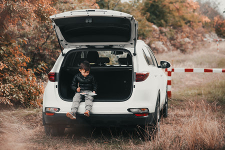 A child is sitting in the trunk of a car SUV or crossover with gouache paints, a car in the autumn forestの写真素材