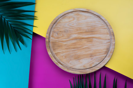 A versatile wooden serving board perfect for pizzas, cheese platters, and more, presented on a colorful tropical background, ideal for modern food photographyの写真素材