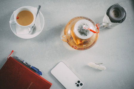 A flat lay of tea, teapot, and daily essentials like a notebook and phone, perfect for productivity...